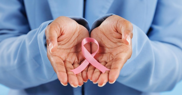 Hands pink ribbon and breast cancer support with awareness and healthcare icon on blue background Person in studio medical symbol and wellness with care trust and kindness in solidarity campaign