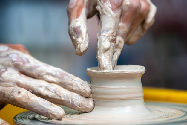 Hands of the potter makes pottery dishes on potter's wheel