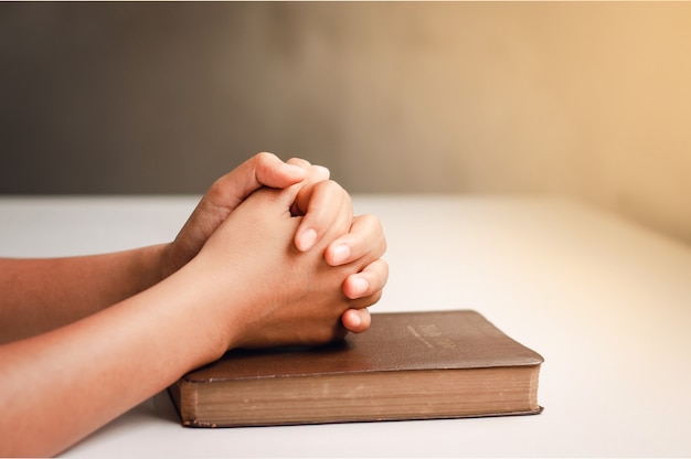 Руки молятся над библией на белом столе крупным планом