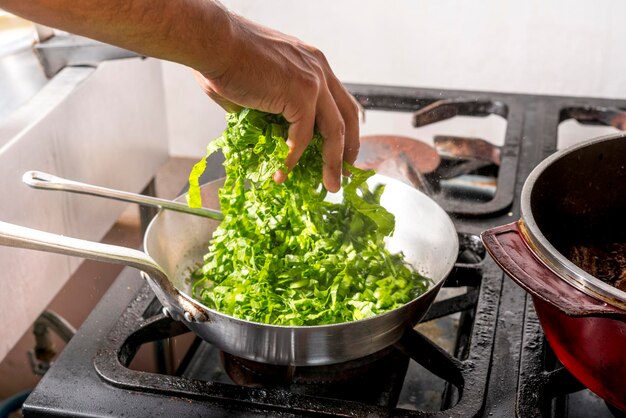 Hands preparing kale in frying pan over stove