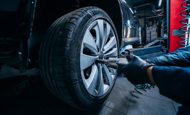 Hands of professional car mechanic changing car wheel in auto repair service Close up