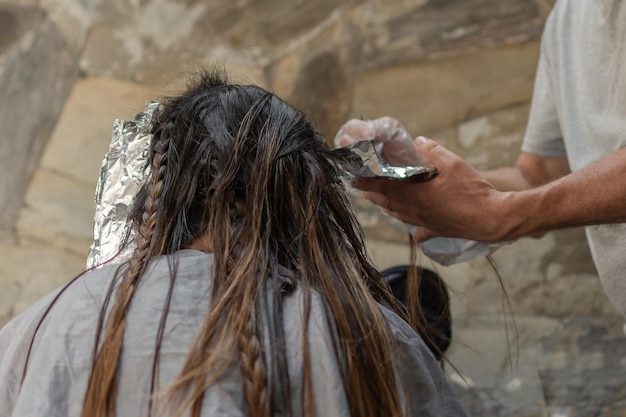 Hands of professional hairdresser dyes hair if her client with brush Selective focus