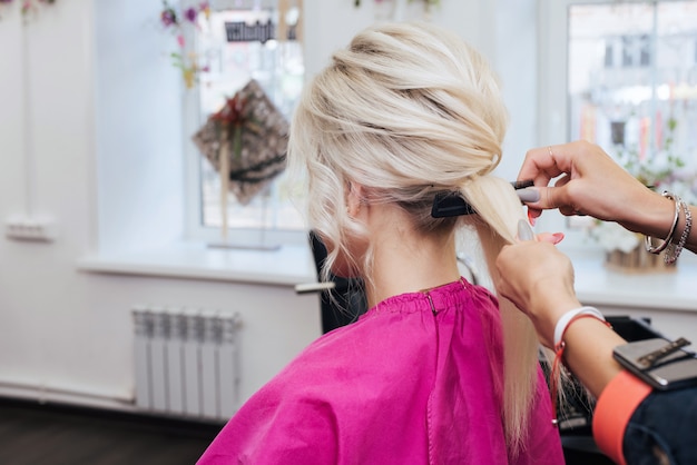 Foto le mani di un parrucchiere professionista fanno un'acconciatura per una ragazza bionda con i capelli lunghi