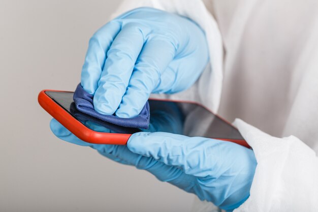 Hands in protective gloves cleaning phone from dust and infection