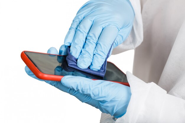 Hands in protective gloves cleaning phone from dust and infection