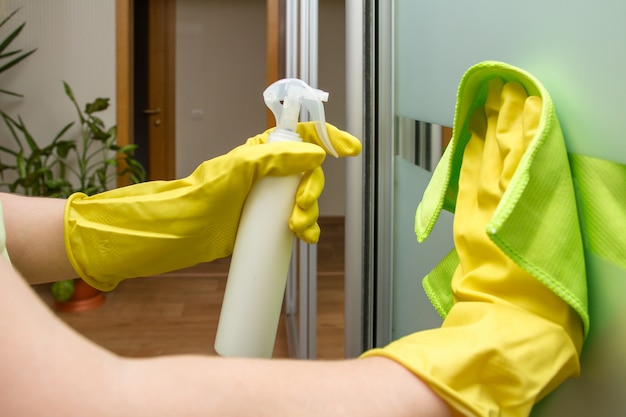 Hands in protective gloves with rag and spray are cleaning the glass wardrobe