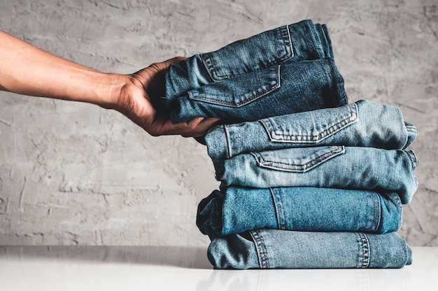 Photo hands, put the stack of blue jeans on gray background.