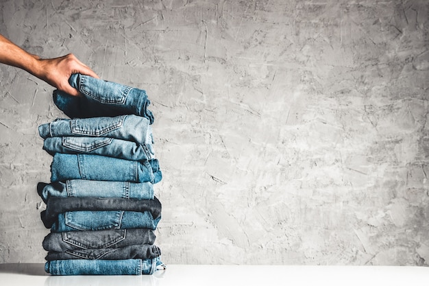 Photo hands, put the stack of blue jeans on gray background.