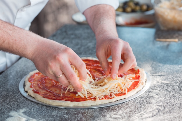 Hands putting cheese on pizza dough