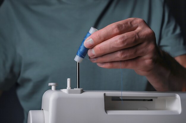 Hands putting thread spool on sewing machine close up