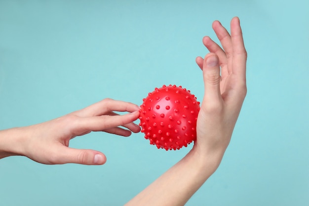 Hands relax with red massage ball on blue. Antistress toy