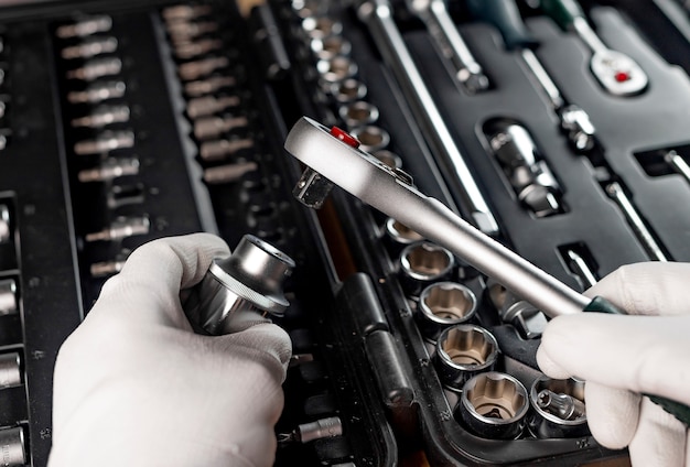 Hands of repairman in gloves close up with metal steel socket ratchet handle over toolbox, POV.