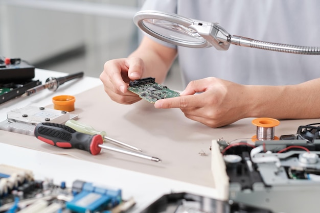 Hands of repairperson with circuit boad of electronic device