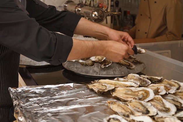 Hands of a restaurant chef preparing dishes and snacks with oysters in the kitchen indoors