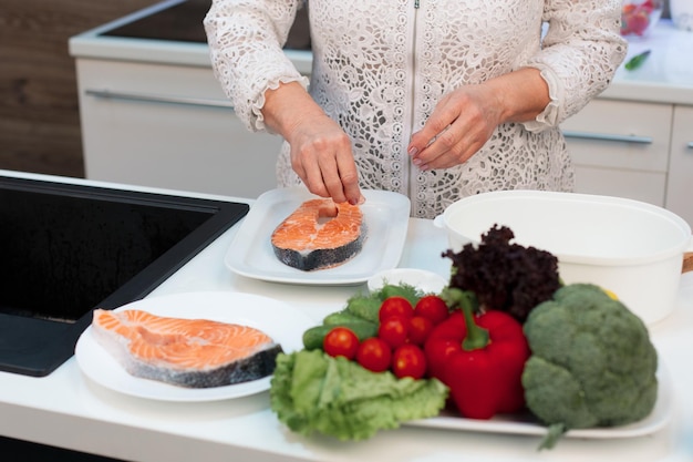 The hands of a retired woman cook red salmon fish in the kitchen salt it and add spices