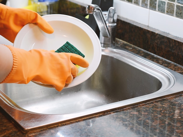 Hands in rubber gloves washing dishes with spon