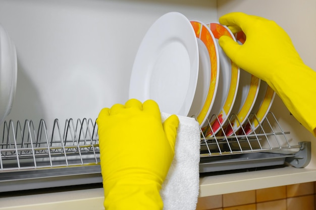 Руки в резиновых перчатках вытирают посуду на кухне при уборке дома