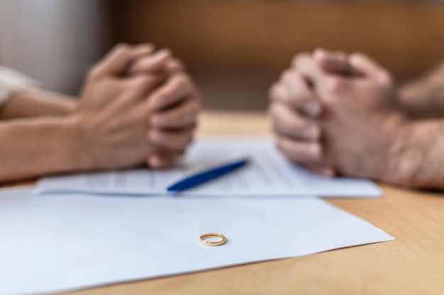 Hands of sad middle aged european man and woman on divorce papers and ring on table agree to breakup