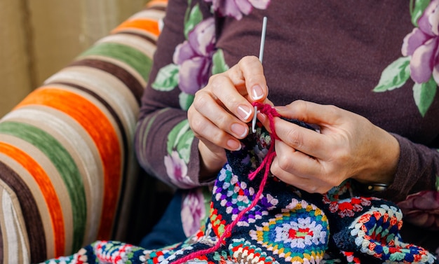 Photo hands of senior woman knitting a vintage wool quilt with colorful patches