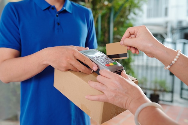 Hands of senior woman swiping credit card to pay courier for package delivery