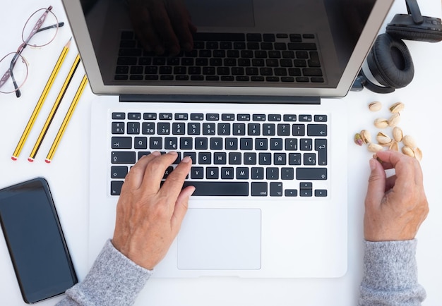 Hands of senior woman working on laptop on white desk Some dry fruit to make a break