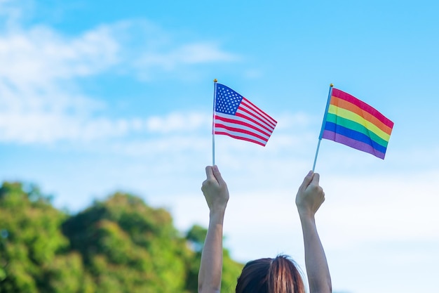 Hands showing LGBTQ Rainbow and America flag on nature background Support Lesbian Gay Bisexual Transgender and Queer community and Pride month concept