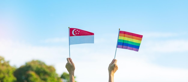 Hands showing LGBTQ Rainbow and Singapore flag on nature background Support Lesbian Gay Bisexual Transgender and Queer community and Pride month concept