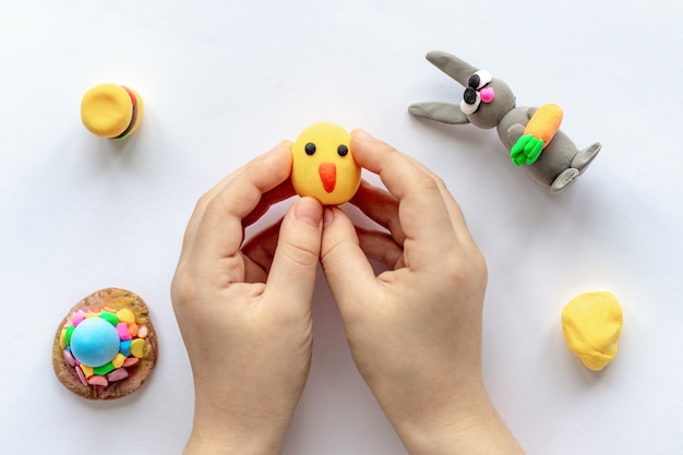 The hands of a small child are holding a yellow plasticine chicken