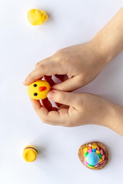 The hands of a small child are holding a yellow plasticine chicken