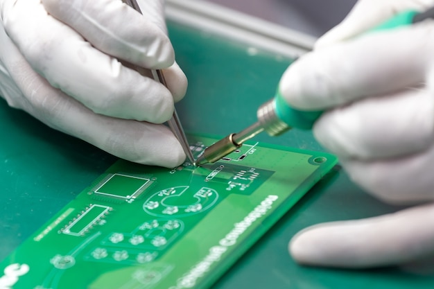 Hands solder components onto a printed circuit board using copper and a soldering iron.