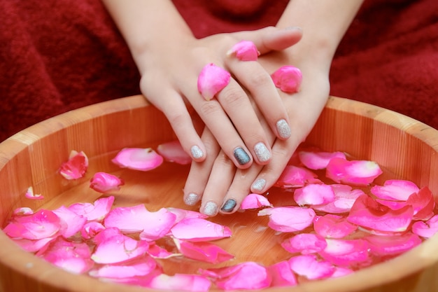 Hands spa manicure in wooden bowl with rose petals