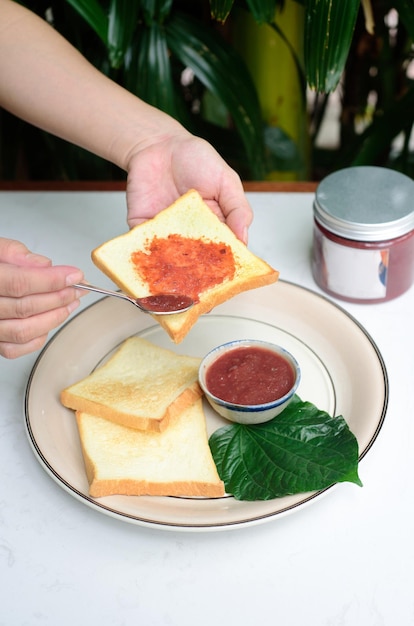 Hands spreading plum jam on a toast against jar with jam and hibiscus flowers