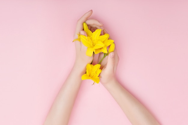 Hands and spring flowers are on a pink table skincare. Nature Cosmetics for hand skin care, a means to reduce wrinkles on hands, moisturizing. Natural cosmetics from flower extract, beauty and fashion