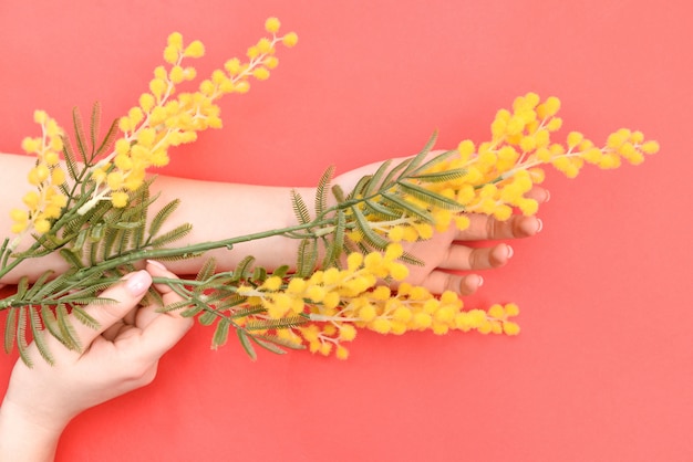 Foto le mani ed i fiori gialli della molla sono su una cura della pelle rossa della tavola. cosmetici naturali da estratto di fiori