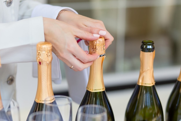 Hands of the steward opening bottles of champagne at the wedding ceremony