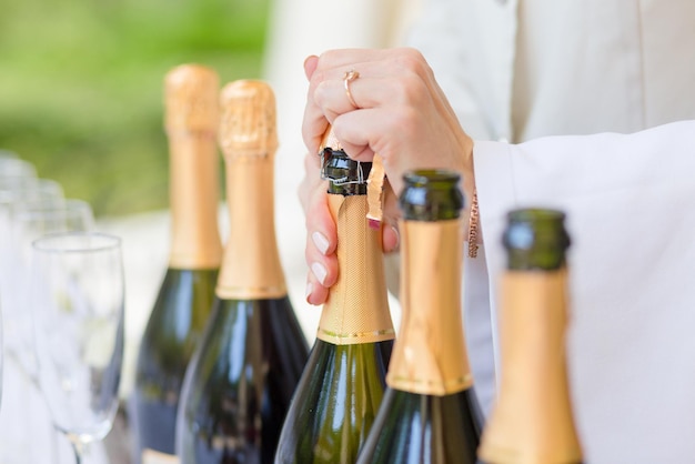 Hands of the steward opening bottles of champagne at the wedding ceremony