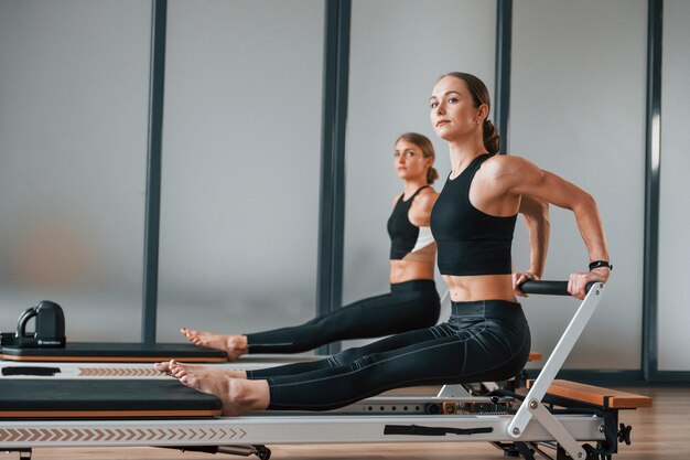 Photo hands strength two women in sportive wear and with slim bodies have fitness yoga day indoors together