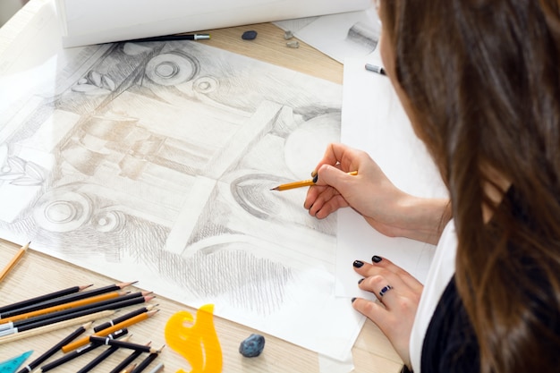 The hands of the student architect with a pencil preparing a pattern of light and shadow, design baluster closeup on a wooden table