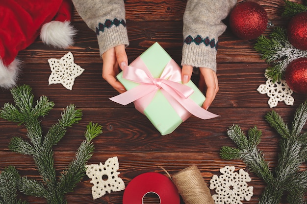 Hands in sweater holding a gift on wooden table with Christmas decorations