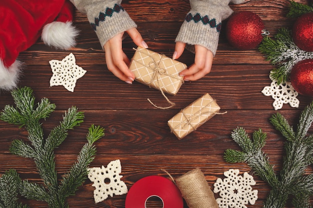 Hands in sweater holding a gift on wooden table with Christmas decorations