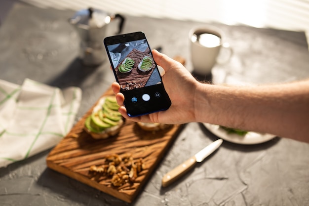 Hands take pictures on smartphone of two beautiful healthy sour cream and avocado sandwiches lying