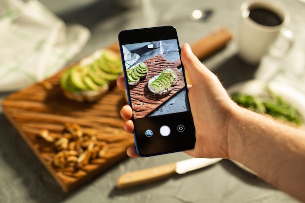 Hands take pictures on smartphone of two beautiful healthy sour cream and avocado sandwiches lying