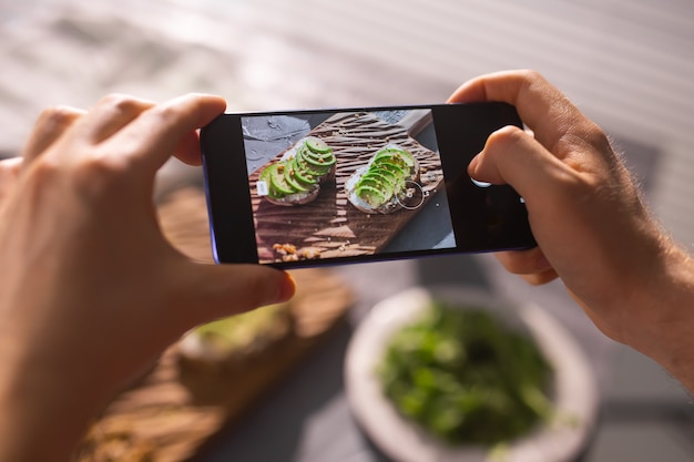 Hands take pictures on smartphone of two beautiful healthy sour cream and avocado sandwiches lying