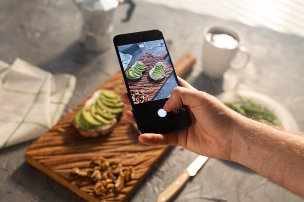 Photo hands take pictures on smartphone of two beautiful healthy sour cream and avocado sandwiches lying