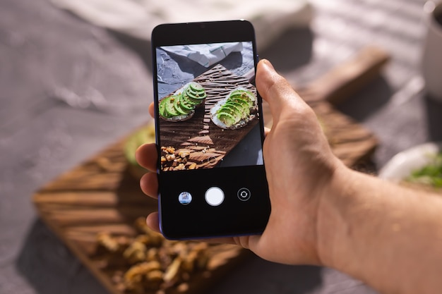 Hands take pictures on smartphone of two beautiful healthy sour cream and avocado sandwiches