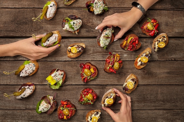 Photo hands taking bruschettas with various toppings on wooden surface