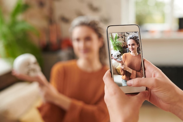 Hands taking photo of pretty young woman with dreads posing with skull at halloween party