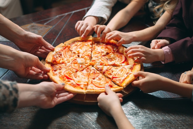 Hands taking pizza slices from wooden table, close up view.