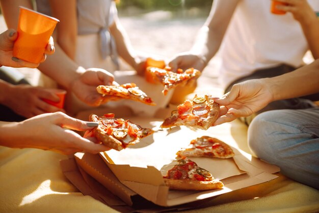 Photo hands taking slices of pizza close view group of friends eating pizza at the beach fast food concept