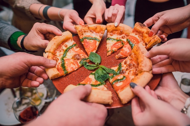 Hands taking slices of pizza